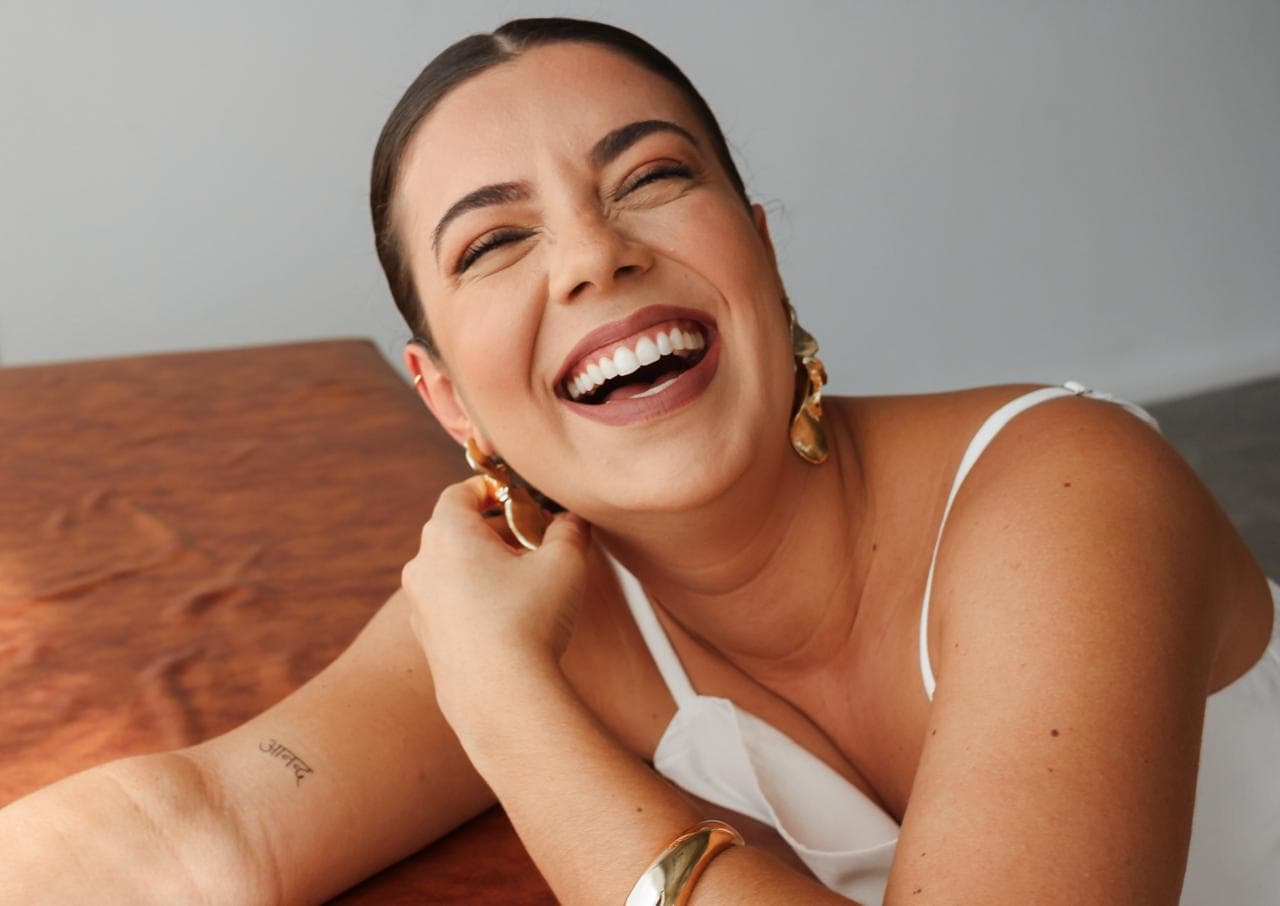 Dra. Thati Garcia, fisioterapeuta pélvica em Curitiba, sorrindo apoiada em mesa de madeira